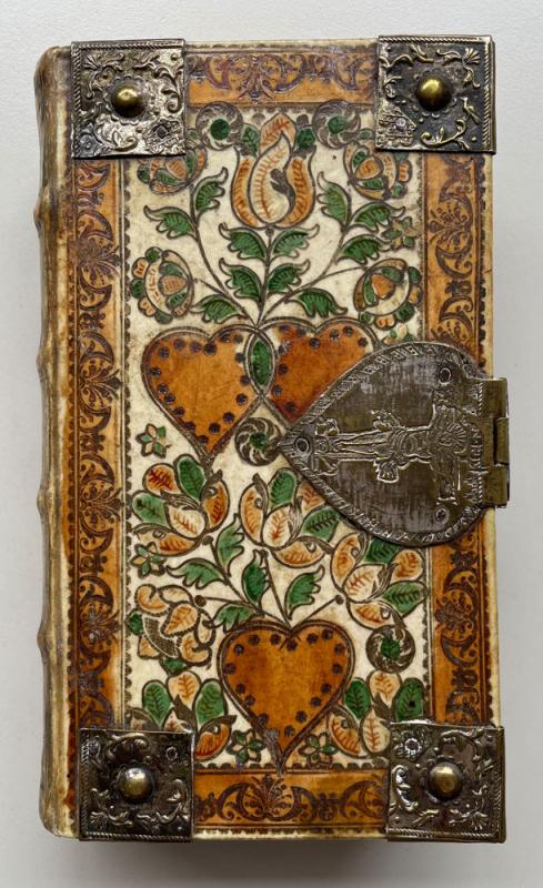 Book binding decorated with hearts and floral patterns in green and earth tones wih herat-shaped metal clasp on right.
